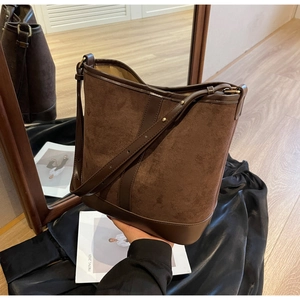 Detail of a large brown suede bucket bag with leather trim on black satin fabric