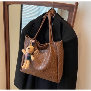 Brown woven tote bag detail featuring a cute checkered rabbit plush charm on a long handle