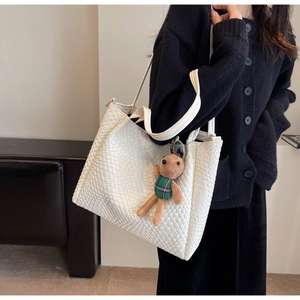 Detailed close-up of white woven tote bag with a cute plush bunny charm and shoulder strap