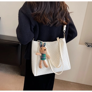 Detail of white woven tote bag featuring checkered texture and brown rabbit charm