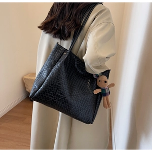Detail of black faux crocodile tote bag featuring a cute plush bunny charm on the strap