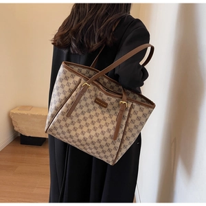 Classic patterned tote bag with brown leather handles worn by model in minimalist room