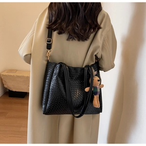 Detail of black woven tote bag featuring a textured finish and a cute bear bag charm