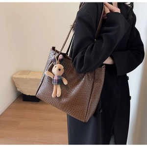 Detail of dark brown tote bag featuring crocodile pattern texture and a plush bunny charm