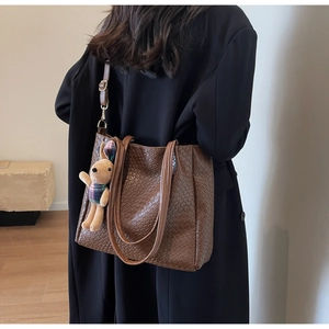 Detailed view of a brown embossed leather tote bag with a cute rabbit plush pendant