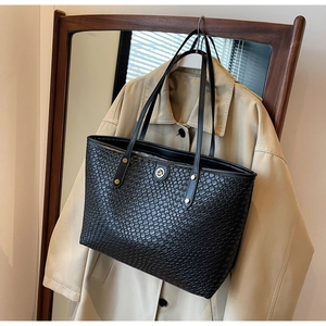 Détail du grand sac cabas noir à texture tressée avec un logo métallique rond DM