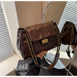 Detail of a brown quilted chain bag featuring a gold metal lock and glossy finish