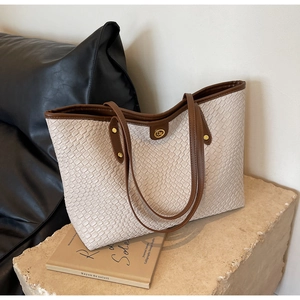Détail du sac cabas en cuir tressé beige avec anses marron et logo métallique doré