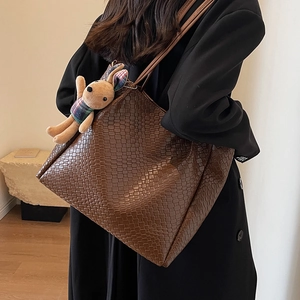 Large brown woven tote bag with cute rabbit charm shown on model in stylish black coat