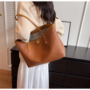 Détail d'un sac cabas tressé marron avec logo doré porté par un mannequin en intérieur