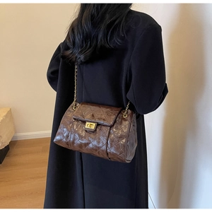 Detail of a deep brown quilted crossbody bag with gold chain strap on a female model