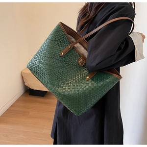 Détail du fourre-tout tissé vert foncé avec lanières en cuir brun et logo métallique