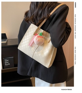 Detail view of cream checkerboard tote bag with brown straps and peach plush pendant