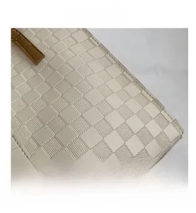 Close-up of beige checkered tote bag fabric with brown leather handle and stitching