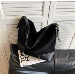 Close-up of black suede tote bag featuring white contrast stitching and adjustable strap