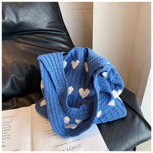Gros plan d'un sac cabas en tricot bleu avec cœurs blancs sur une chaise en cuir et magazine