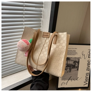 Detail of checkered tote bag with brown straps, fashion label and pink plush charm