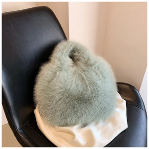 Close-up of fluffy faux fur handbag in light green on a leather chair