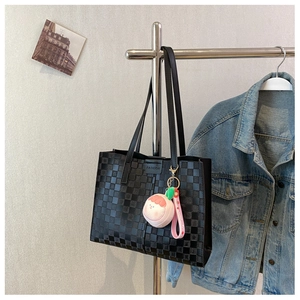 Detail of black checkered tote bag with fashion patch and pink peach plush charm