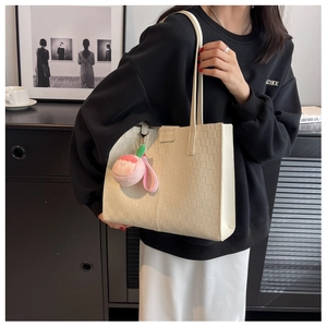 Detail of cream tote bag with checkered texture and peach plush charm decoration