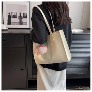 Close-up of cream woven texture tote bag with a pink peach plush pendant on a shoulder strap