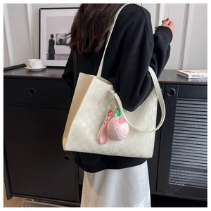 Detail view of large white tote bag with woven PU leather texture and peach plush pendant