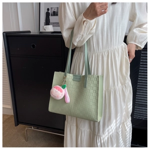 Detail of light green tote bag with checkered texture and peach plush charm on strap