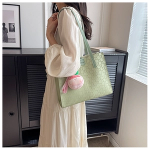 Close-up of light green tote bag with woven texture and a cute pink peach plush charm