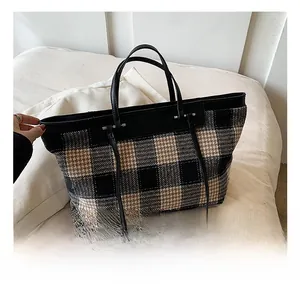 Detailed close-up of large plaid tote bag with black leather straps on soft fabric
