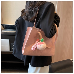 Detail of pink woven leather tote bag with plush charm shown in an office setting