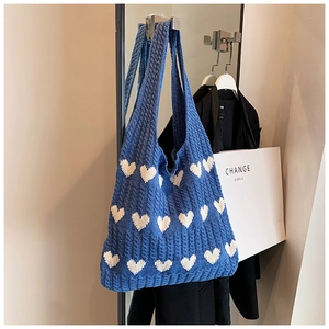 Détail d'un sac cabas en maille bleue avec texture torsadée et motif de cœur blanc tissé