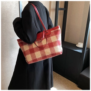 Detail of red and beige checkered canvas tote bag with leather handles on a model