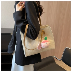 Detail of cream woven tote bag with brown straps and peach plush charm on a shoulder