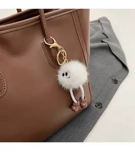 Close-up of fluffy white cartoon plush keychain on a premium brown leather tote bag