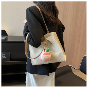 Detail of cream woven leather tote bag with brown strap and peach charm worn by model
