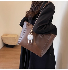 Detail of dark brown leather tote bag with a white plush monster charm accessory