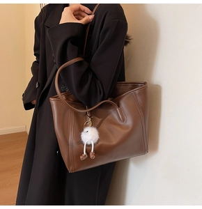 Detail view of large brown tote bag with soft leather texture and white plush pendant