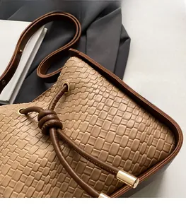 Detail of woven khaki bucket bag featuring brown leather drawstring and golden hardware