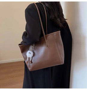 Brown leather tote bag side view with plush charm on a model for daily commuting