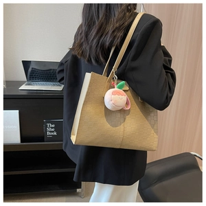 Close-up of beige checkerboard tote bag with peach plush charm in office setting
