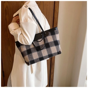 Close-up of a large checkered canvas tote bag worn by a model in white coat