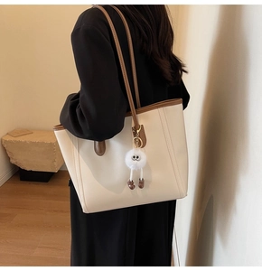 Detailed side view of a large cream tote bag with brown straps and a plush toy charm