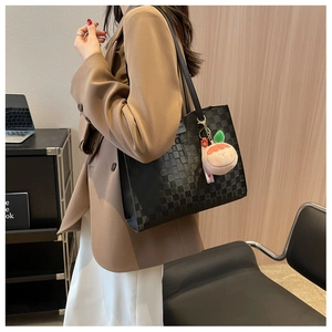 Detail of black checkered tote bag with a peach plush pendant for office commute style