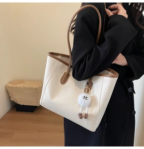 Off-white leather tote bag with brown trim and cute plush charm on a model