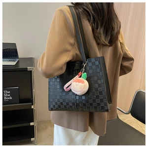 Detail of a black checkerboard tote bag with peach plush charm shown on a shoulder