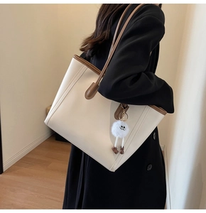 Spacious off-white tote bag with brown trim and a plush charm shown on a shoulder