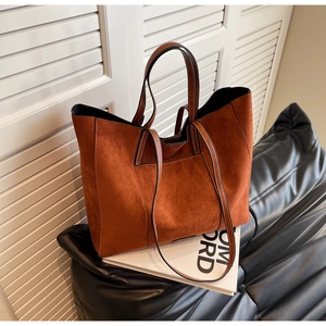 Detail of a brown suede tote bag with leather handles on a sleek black sofa