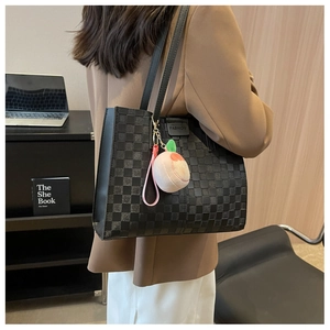 Detail of black checkered tote bag with peach plush charm and fashion leather label