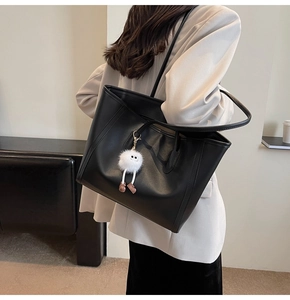 Detailed view of a black oversized tote bag with a cute white plush pendant accessory