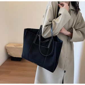 Detail of a black large tote bag with white contrast stitching on a beige trench coat